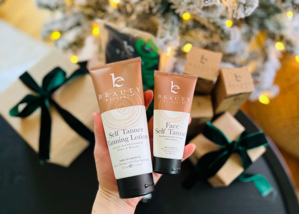 hands holding beauty by earth self tanner products in front of lit christmas tree