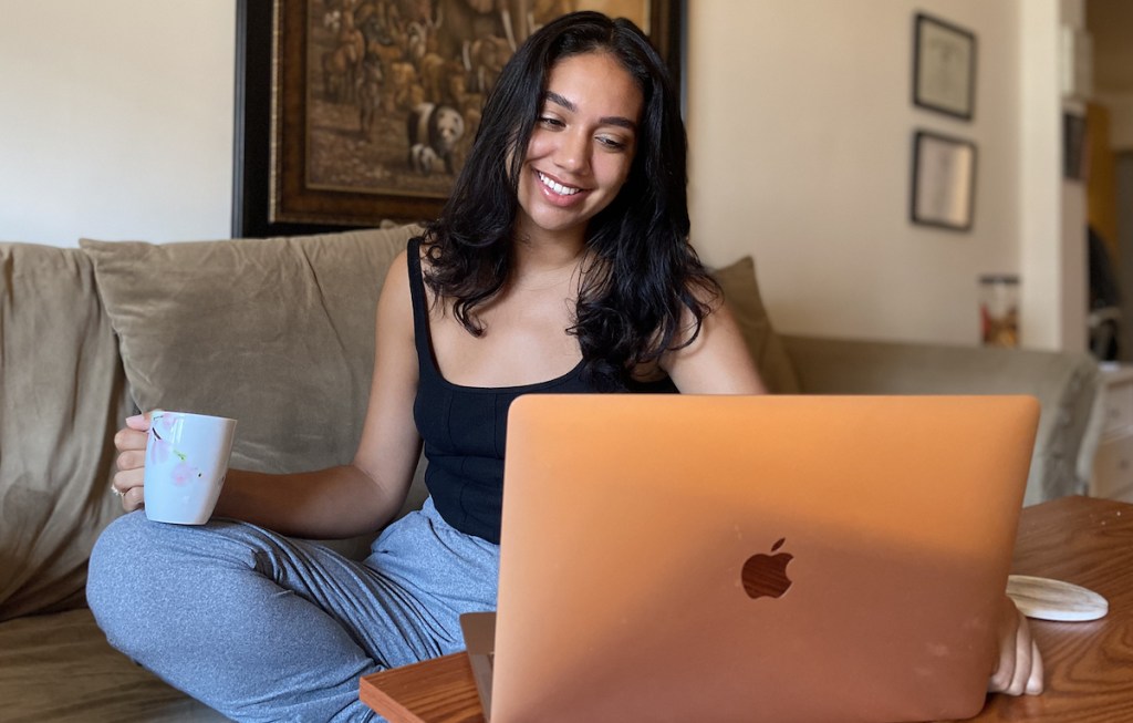 woman sitting in front of apple laptop holding a coffee mug