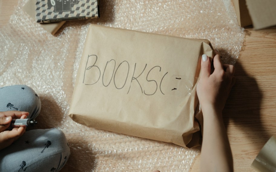 hand holding edge of paper covered gift labeled books for packing tips for moving