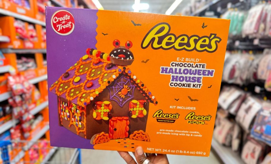 a womans hand holding a reese's halloween house cookie building kit