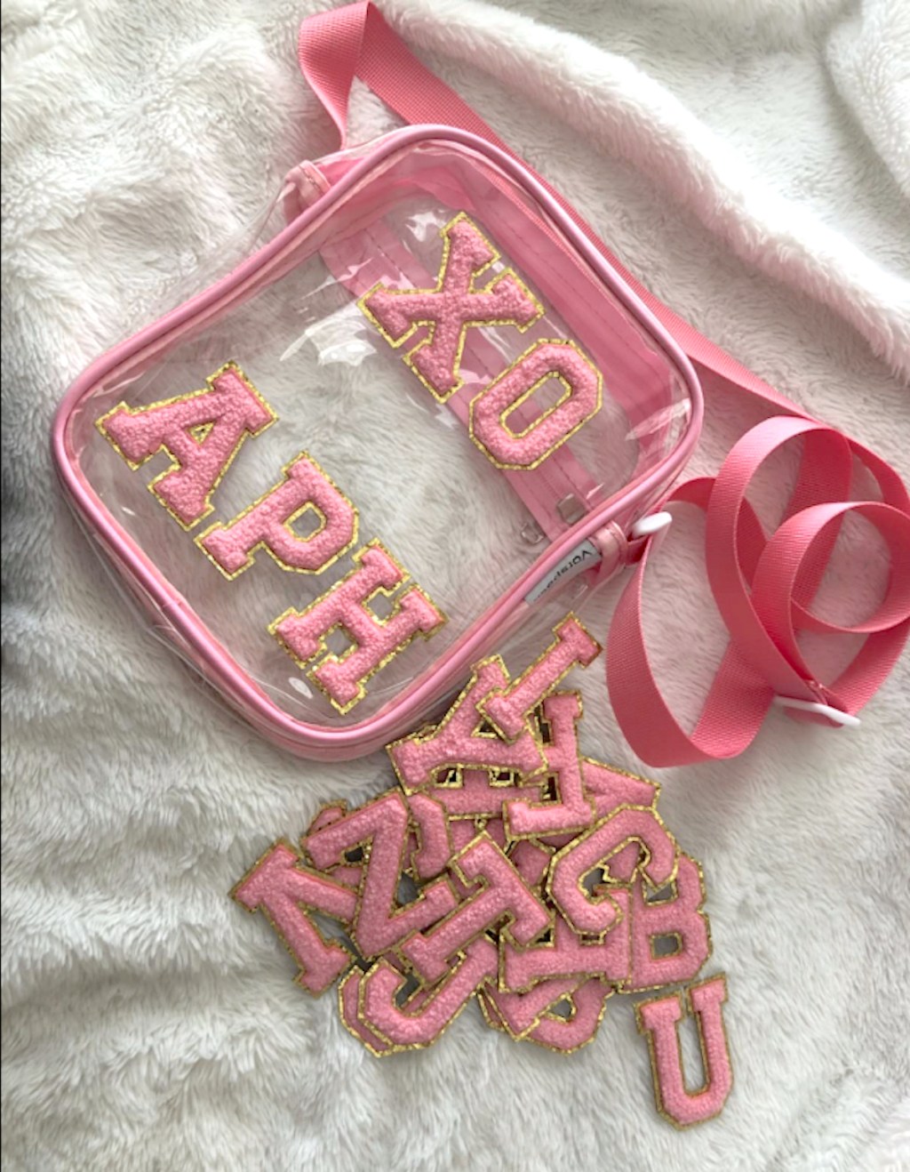 pink letter patches on clear bag laying on white fur blanket