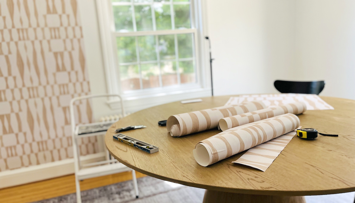 round wood table in dining room with rolls of wallpaper and application tools