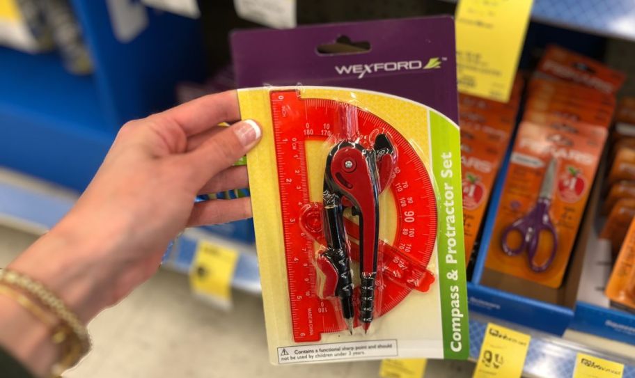 a womans hand holding a packaged compass and protractor