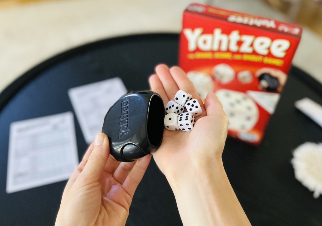 hands holding dice with yahtzee board game in background