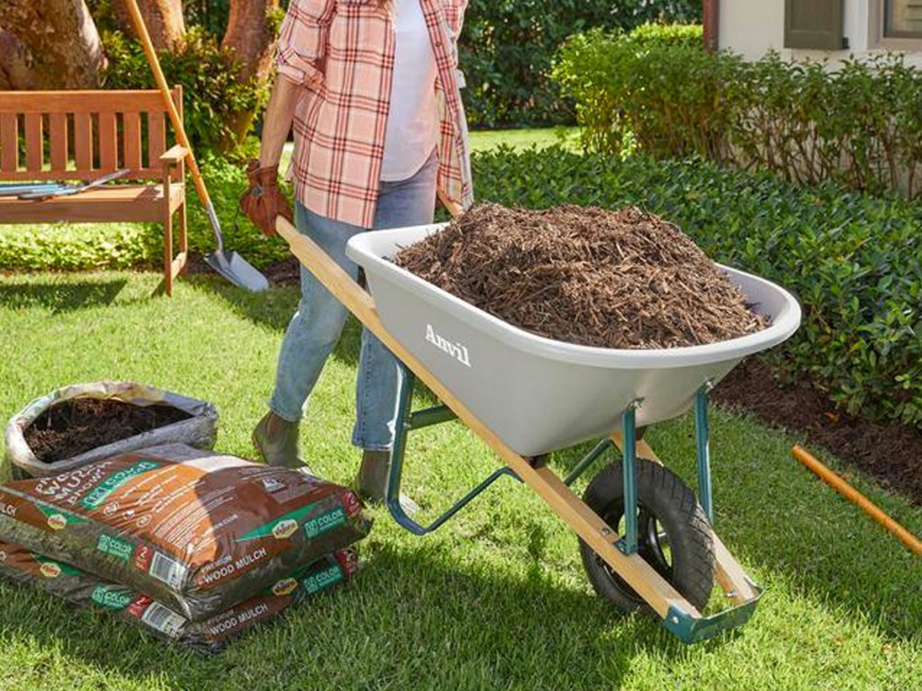 woman using a grey wheelbarrow to move mulch in yard