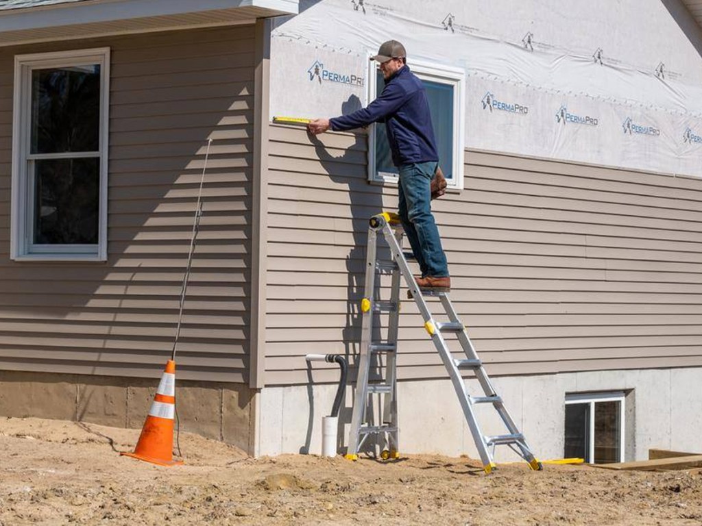 man standing on ladder leaning against side of a house