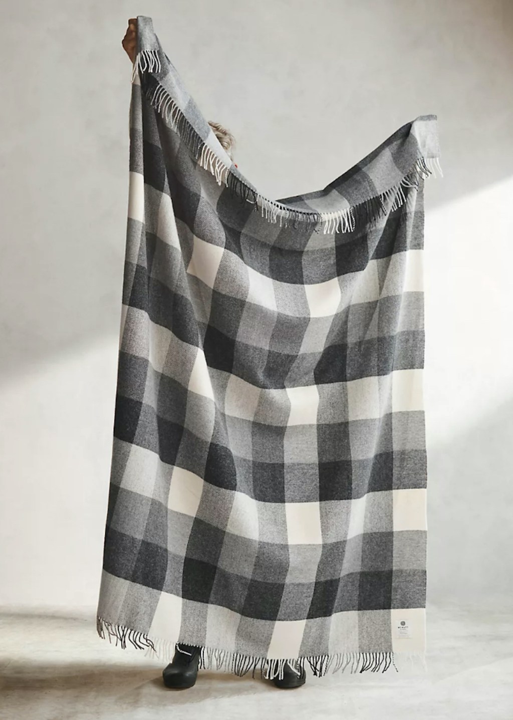 person holding up black gray and cream buffalo plaid check blanket