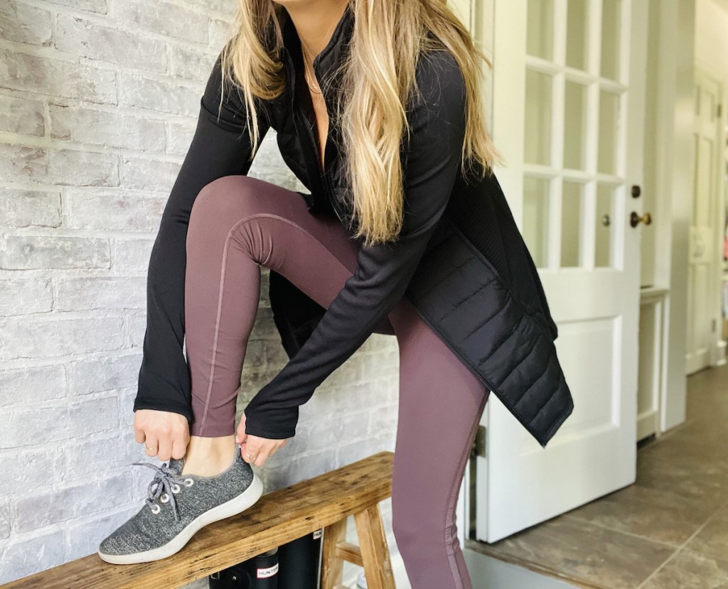 woman putting on shoe standing on wooden bench