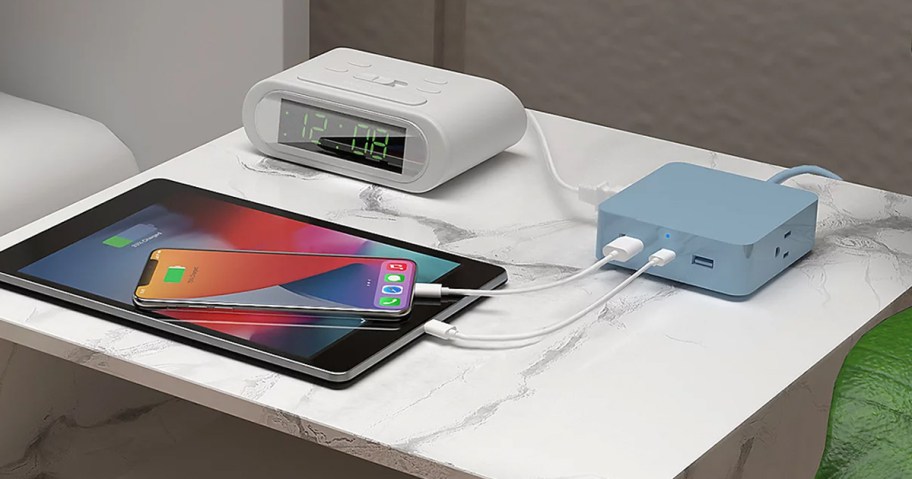 blue charger charging tablet, phone, and alarm clock on nightstand