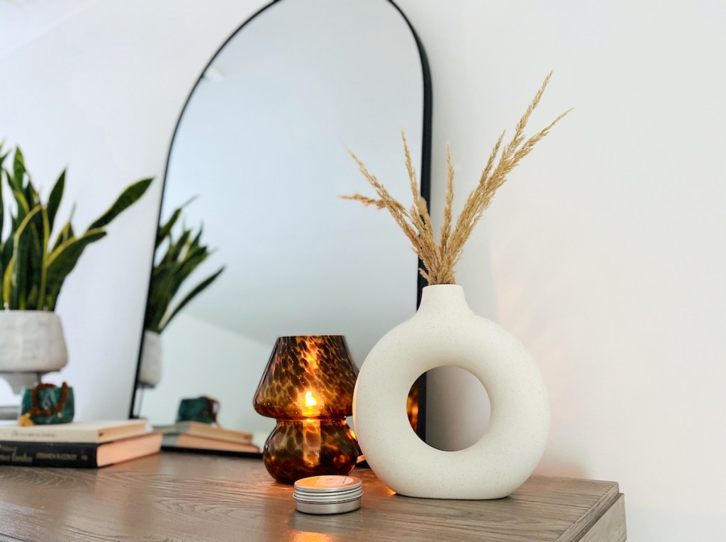 round matte white vase with wheat grass and lit mushroom lamp on dresser with mirror
