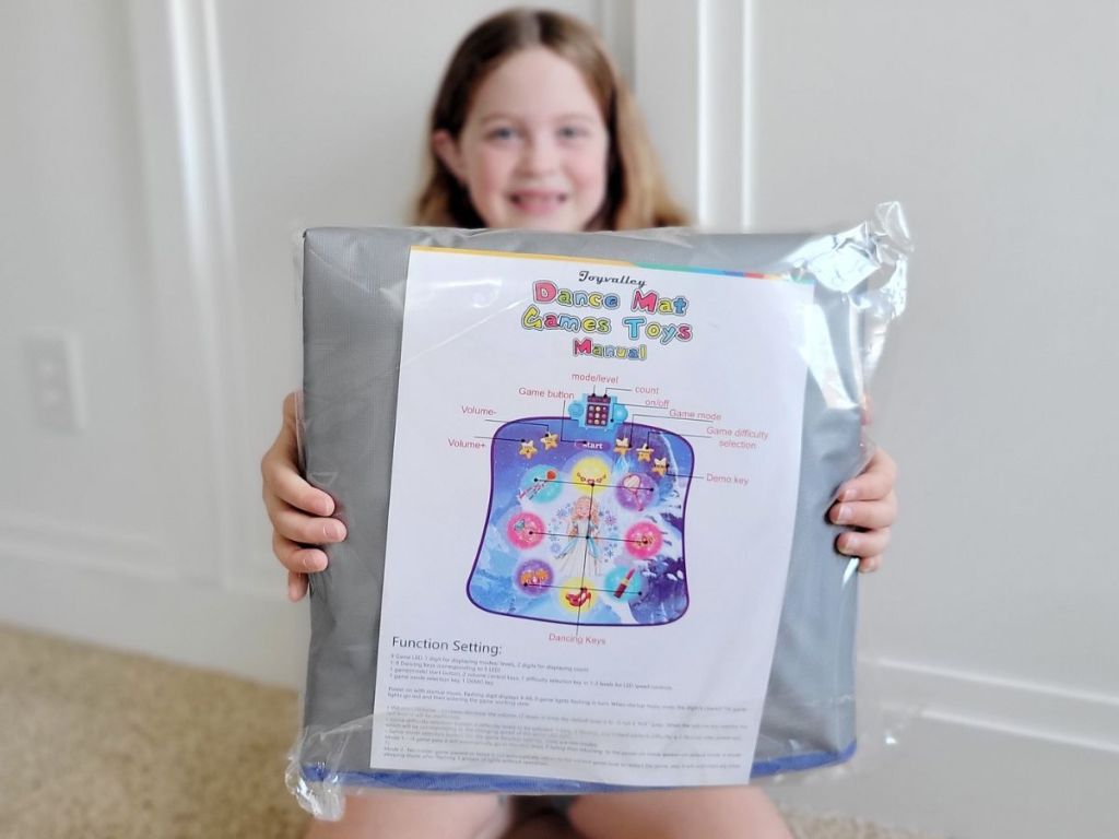 Little girl holding a dance mat toy in the packaging