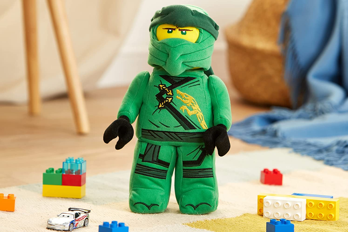 NInjago Lloyd LEGO Plush standing on the floor near some LEGOs and Cars diecast car