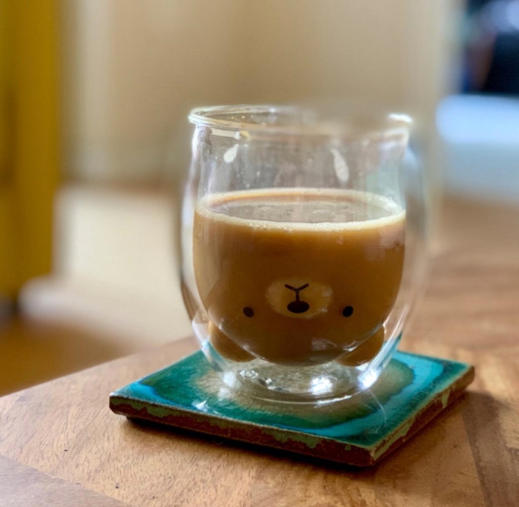 bear shaped double wall glass mug sitting on blue coaster and wood coffee table