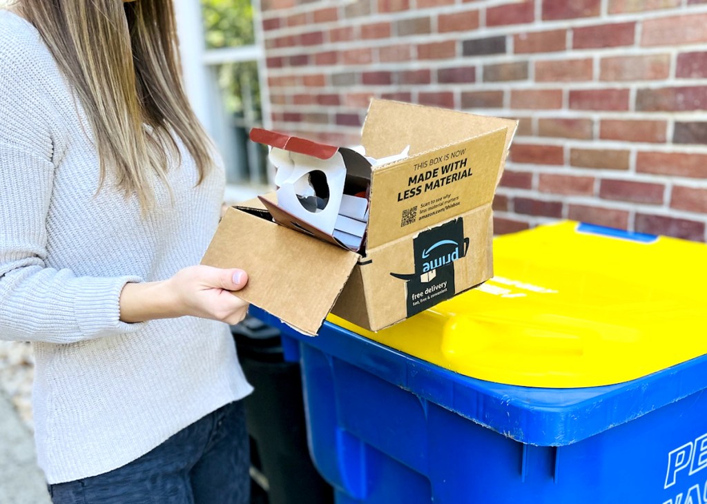 woman holding cardboard box in front of recycle bin