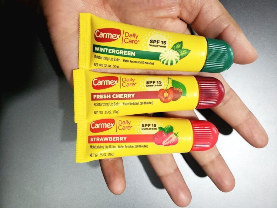 hand holding wintergreen, fresh cherry and strawberry carmex tubes