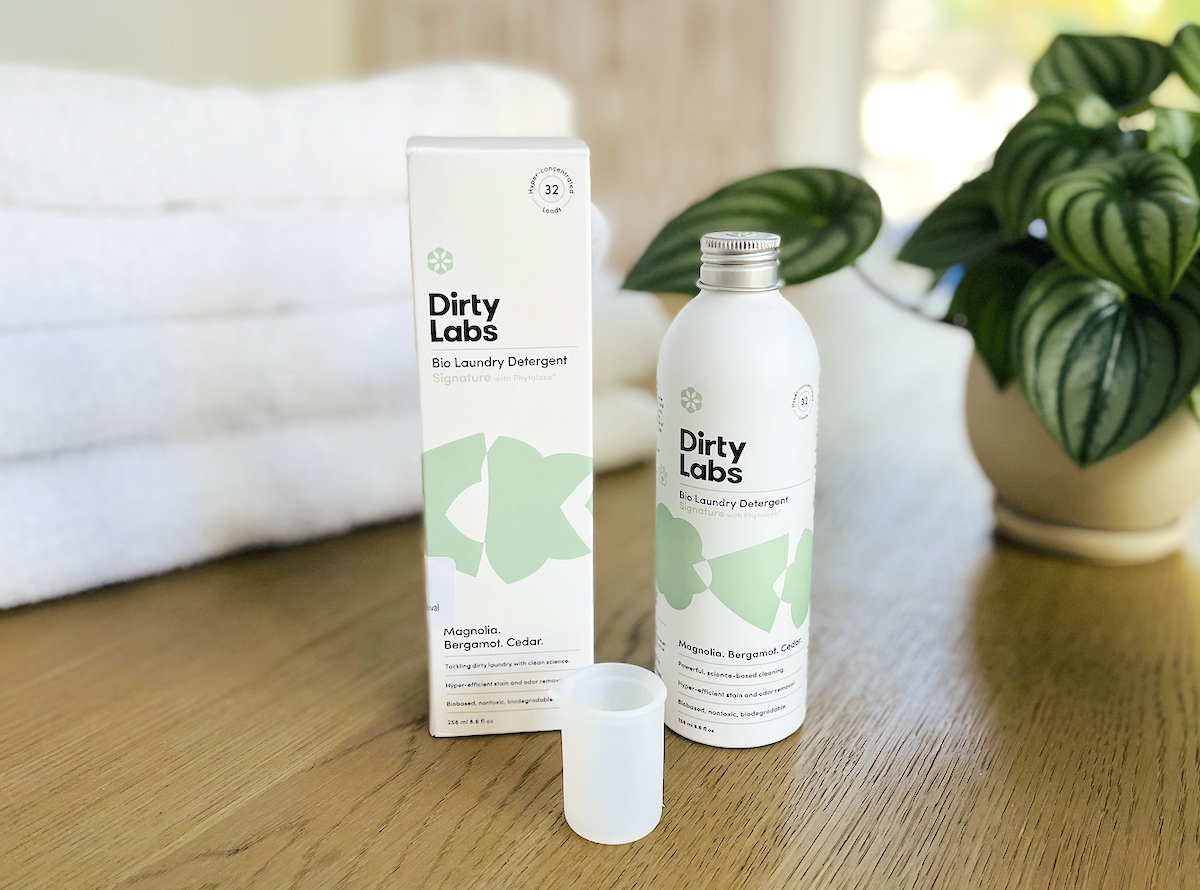 dirty labs laundry detergent bottle and box on wood table with white towels and plant