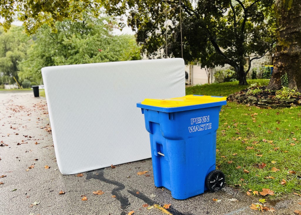 white mattress next to blue recycling bin on side of road