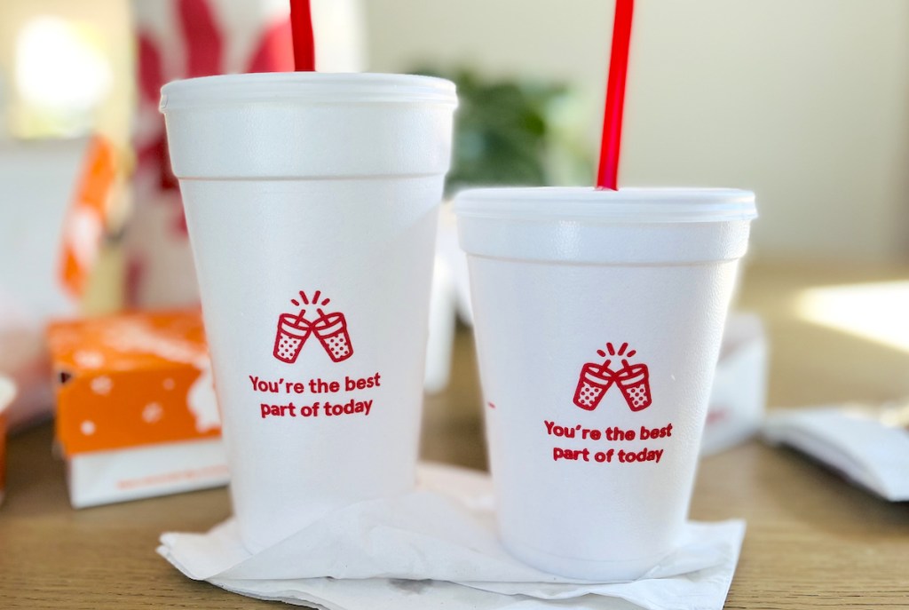 two styrofoam cups sitting on table with takeout food