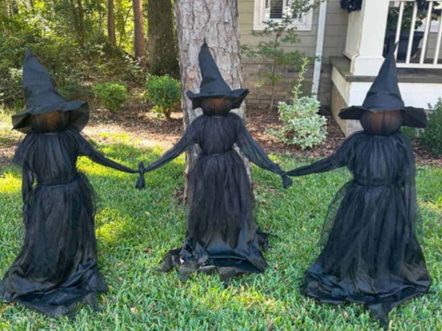 three witches holding hands outside during the day