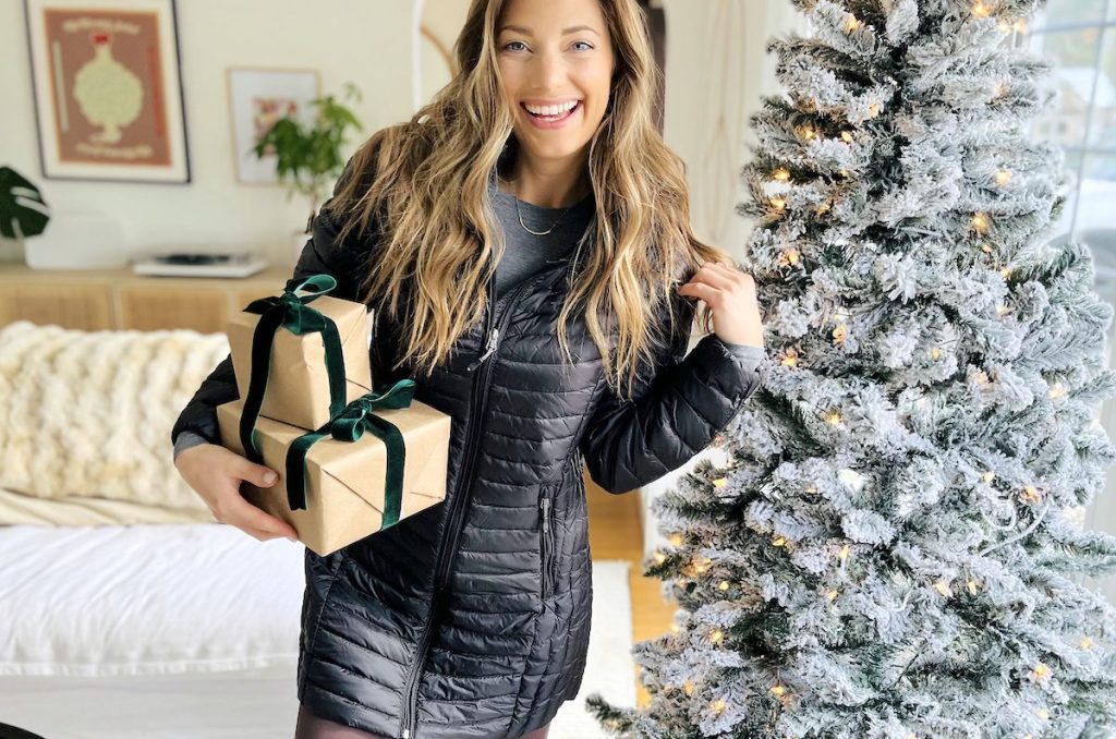 woman standing next to christmas tree holding presents