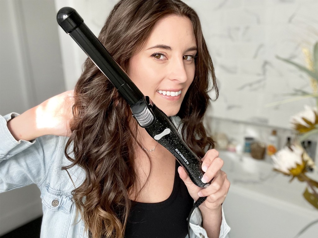 woman with curly hair holding up black curling iron