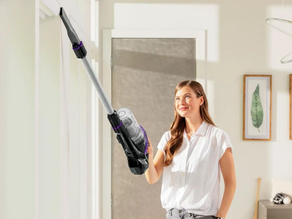 Woman using Bissel Powerglide Pet Eraser Vacuum handheld portion to clean trim overhead