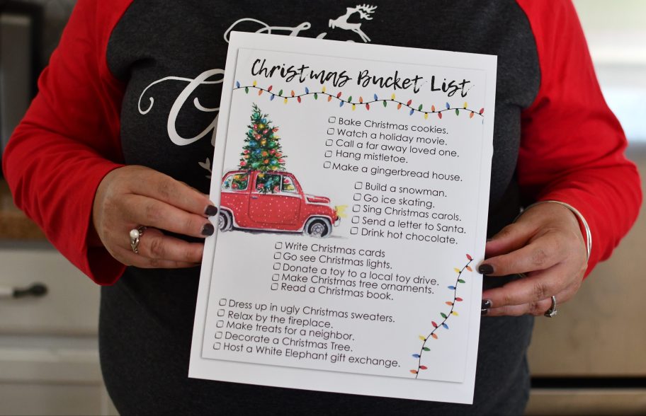 woman holding up a free printable christmas bucket list for the holidays