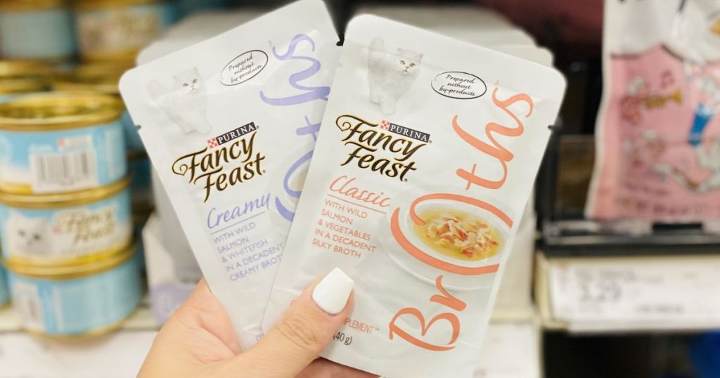 Hand holding two packages of Fancy Feast Broths