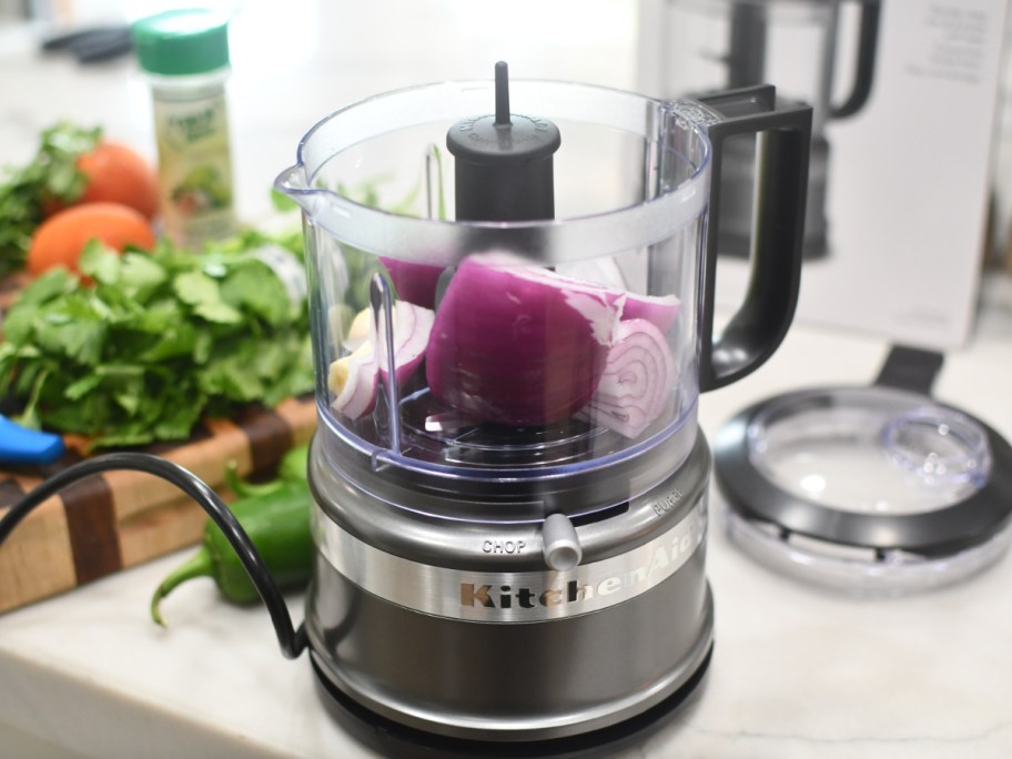 Kitchenaid chopper displayed with onions inside and veggies on the side