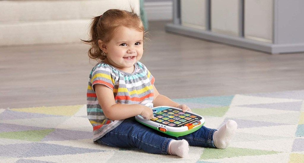 A toddler sitting on the floor and playing with the LeapFrog My First Learning Tablet