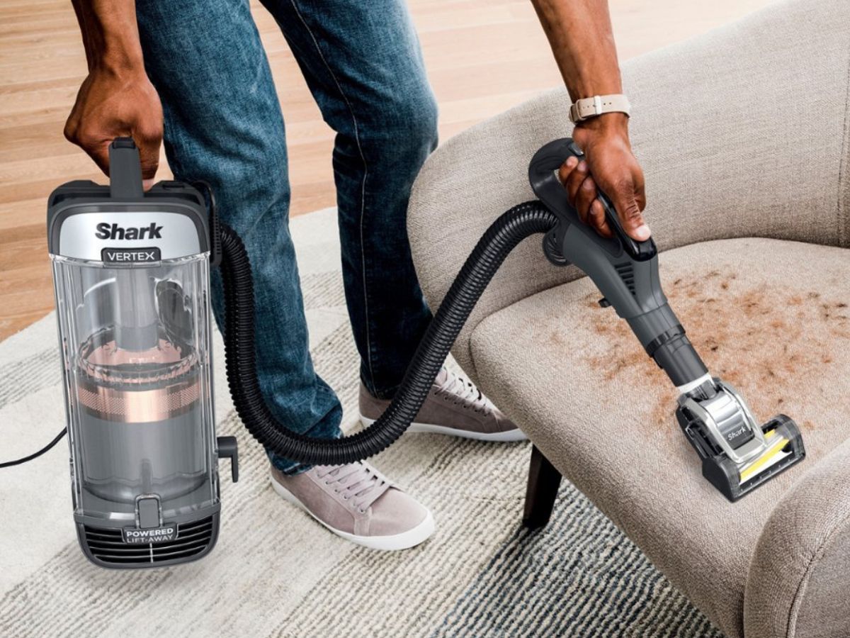 person using shark vertex duoclean vacuum to vacuum chair