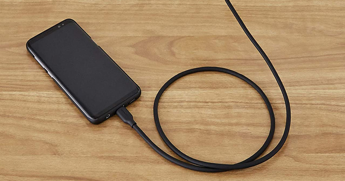 amazon basics charging cable plugged into a black phone on a wooden surface