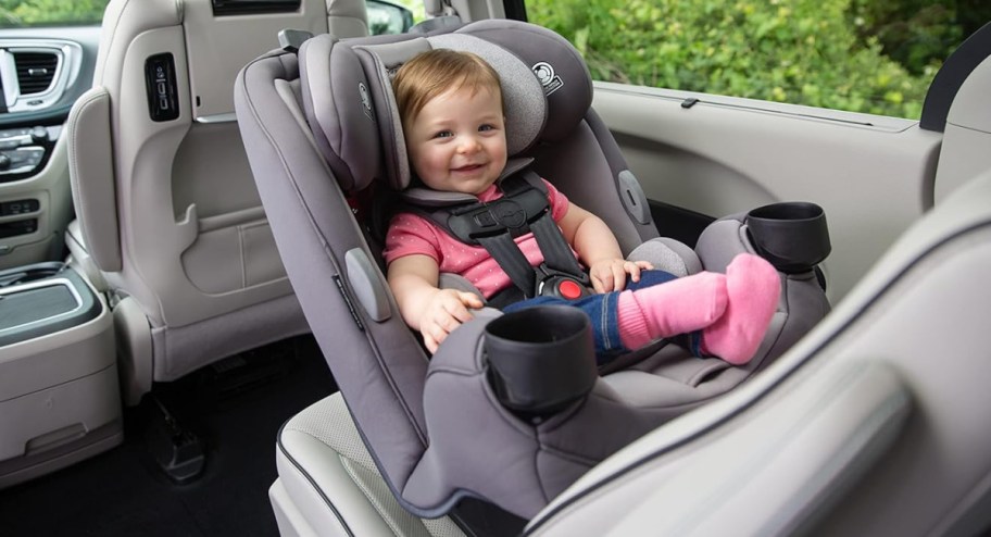 baby sitting in safety 1st car seat in grey in the back of a car