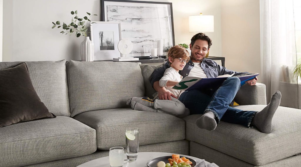 man and boy sitting on sectional couch reading book