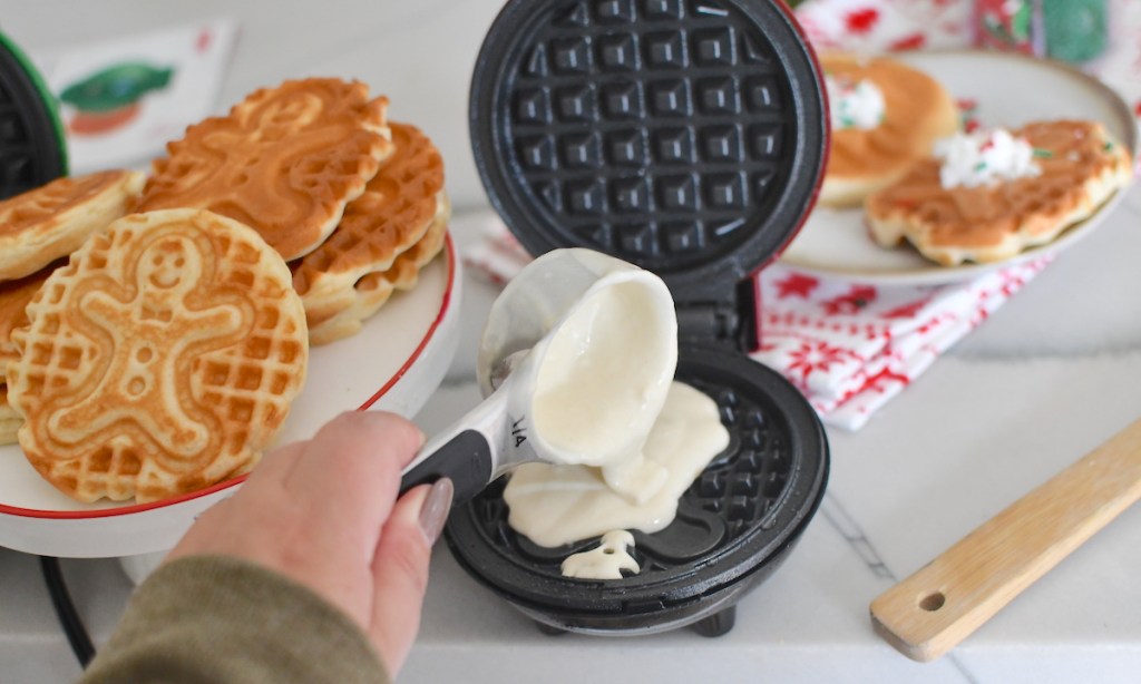 hand pouring waffle batter into waffle maker shaped like a gingerbread