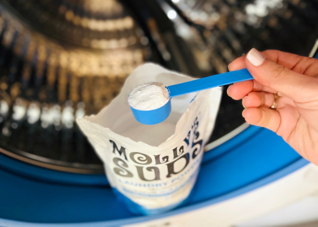 hand holding blue scooper full of white powder in washing machine