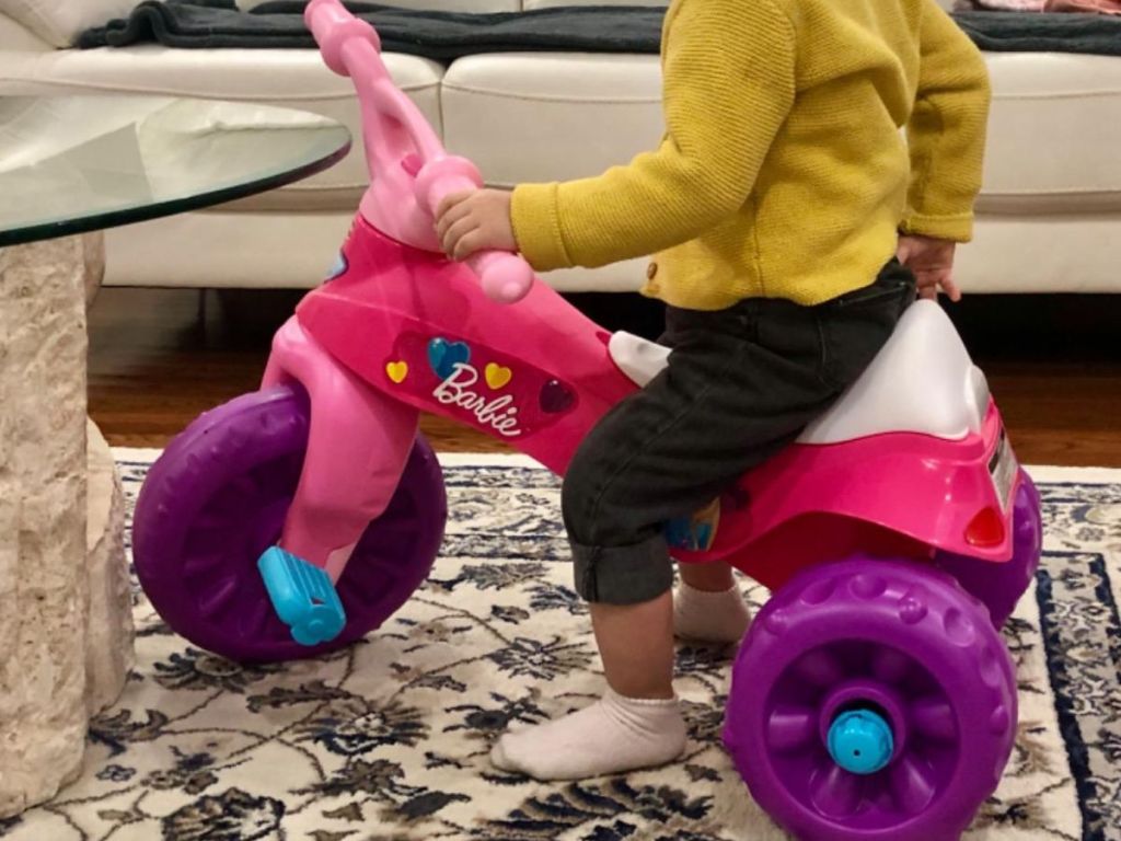 Little girl riding a barbie rough trike in the house