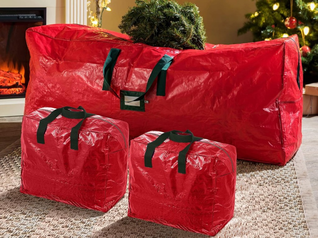 Three red Christmas tree storage bags on rug filled with artificial Christmas tree