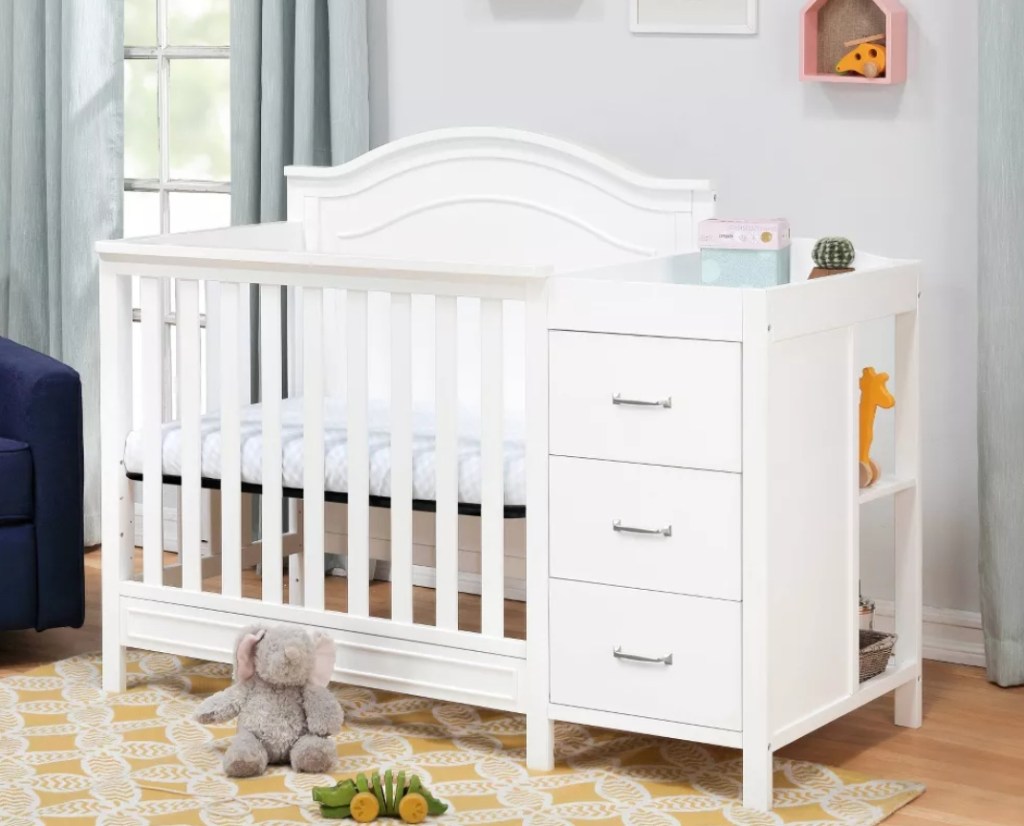 Baby nursery with a white crib and changing table combo and toys on the floor