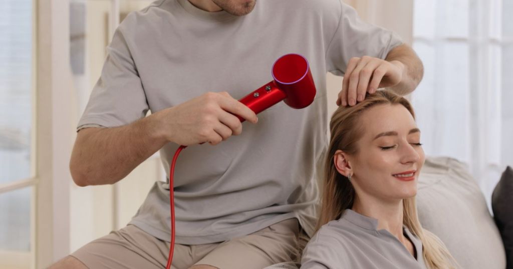 man using red blow dryer on woman's hair