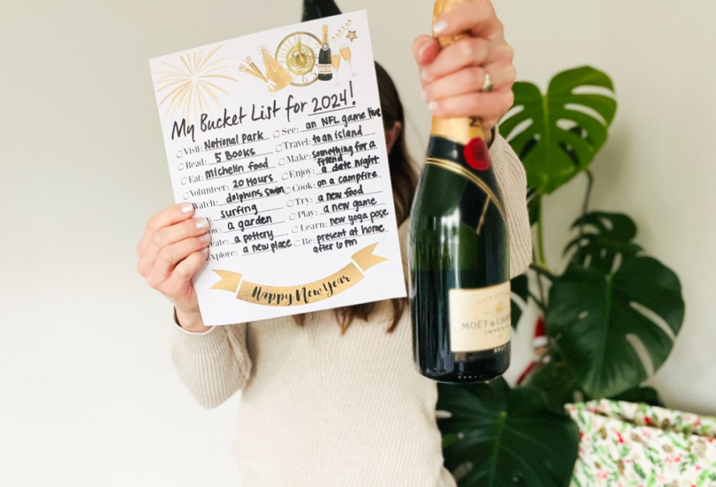 Woman holding up a 2024 New Year's Bucket List and a bottle of Moet & Chandon champagne