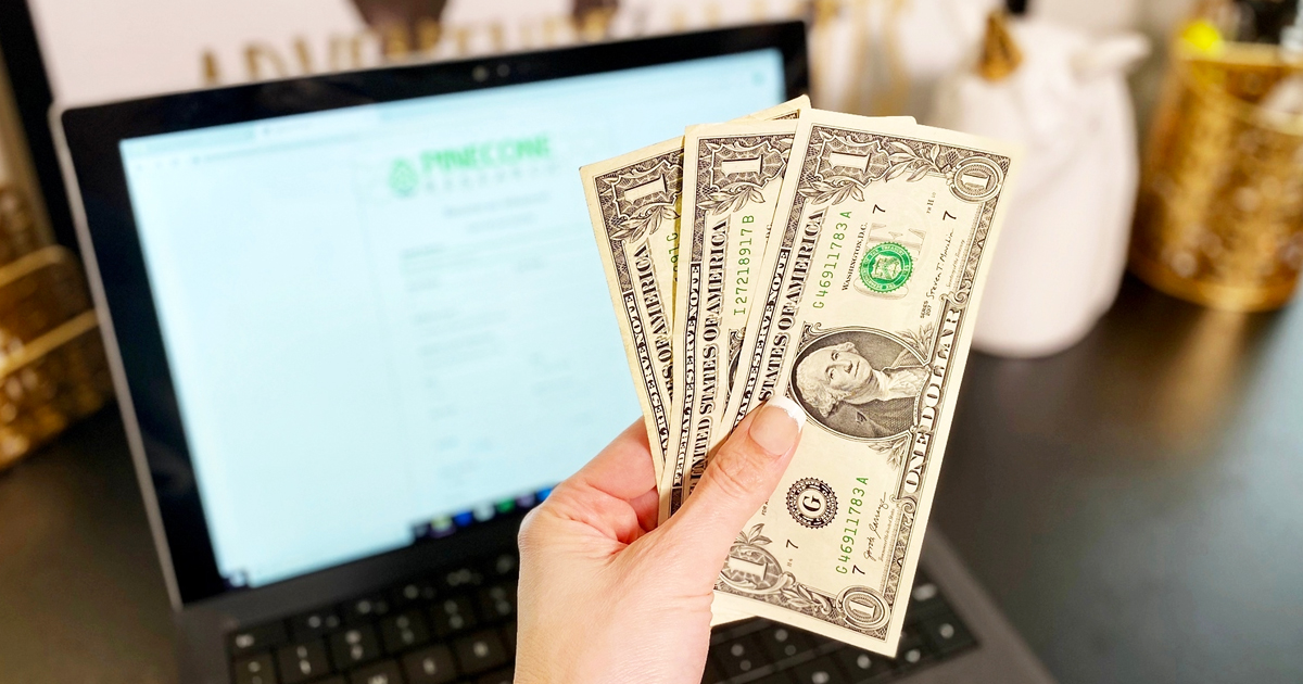 holding up dollar bills in front of laptop