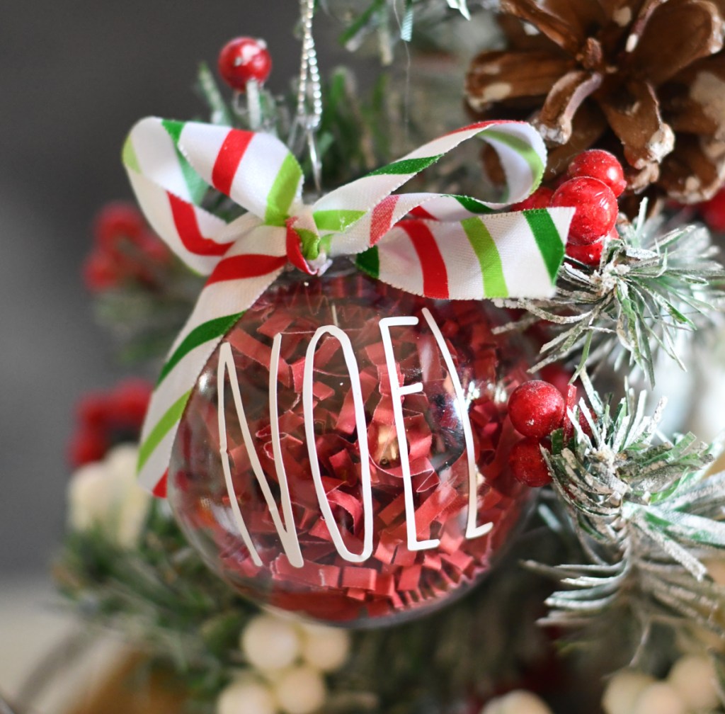 A Rae Dunn DIY CHristmas Ornament that says "Noel" hanging on a tree