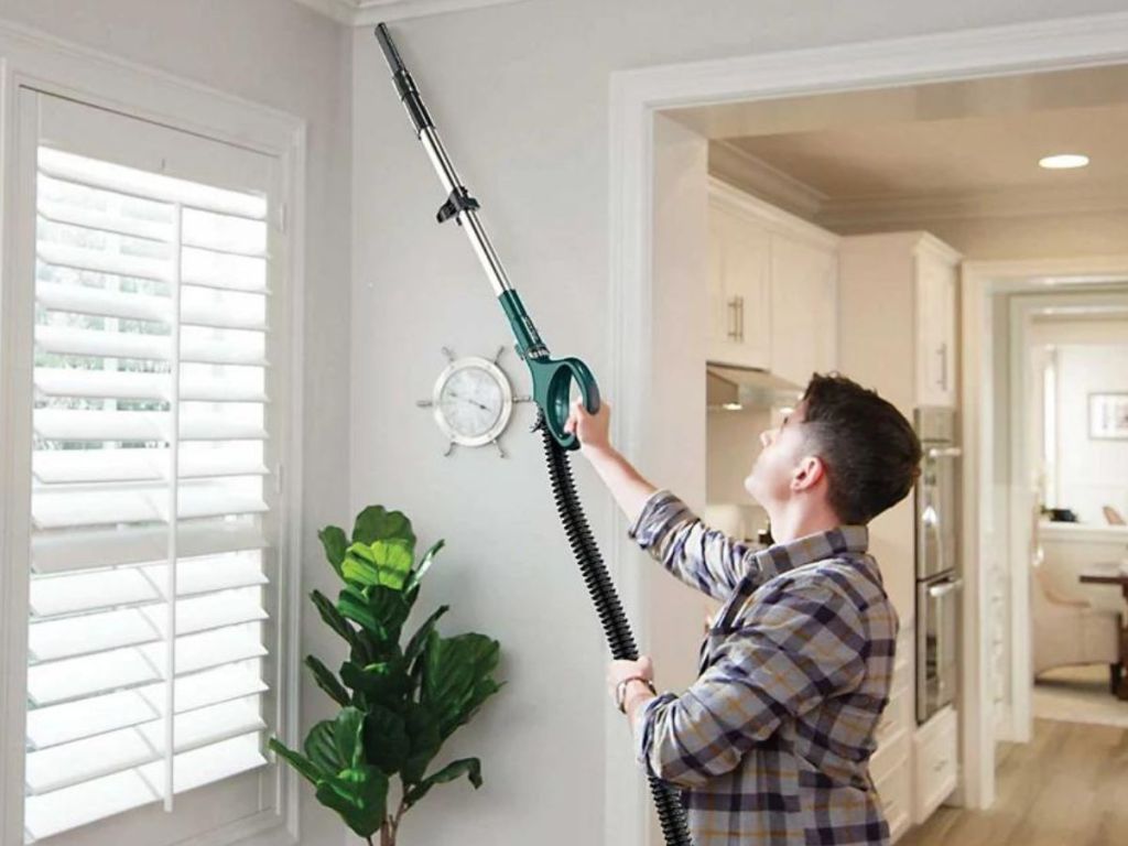 man using vacuum wand on corner of ceiling