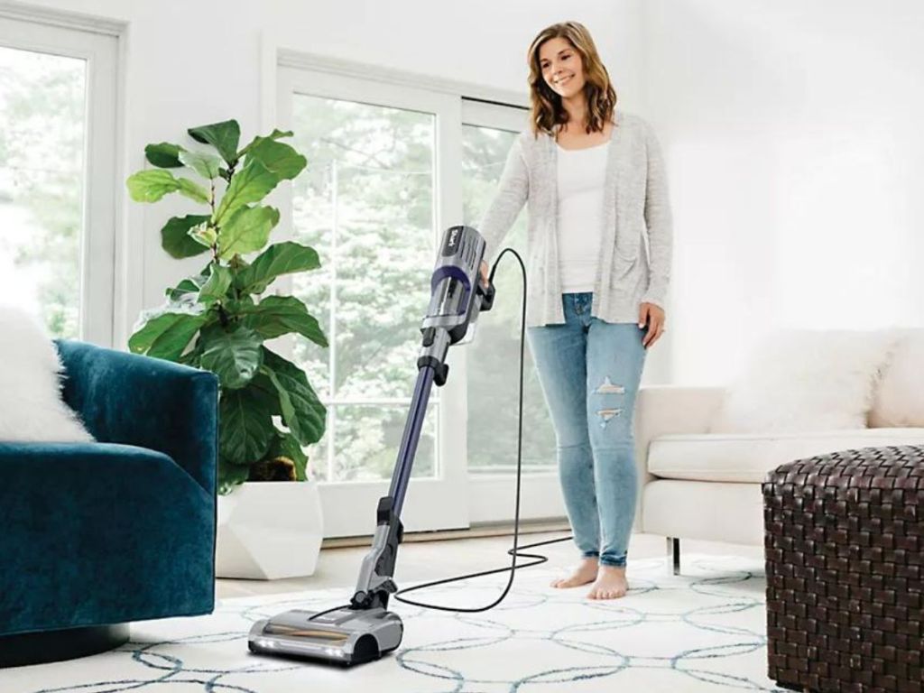 woman using Shark stick vacuum to clean area rug 