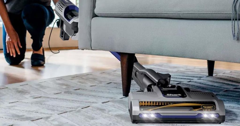 woman using Shark vacuum on carpet under couch