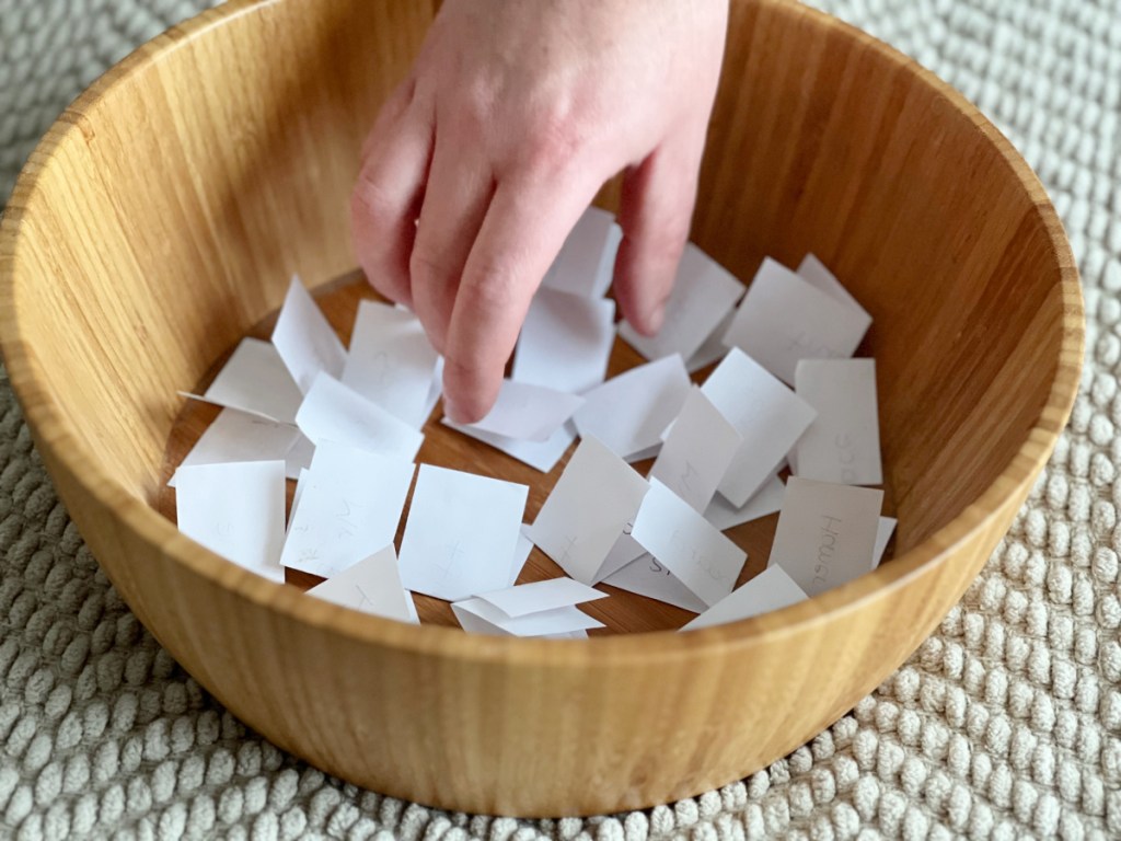 Hand reaching into a container holding The Salad Bowl Game clues