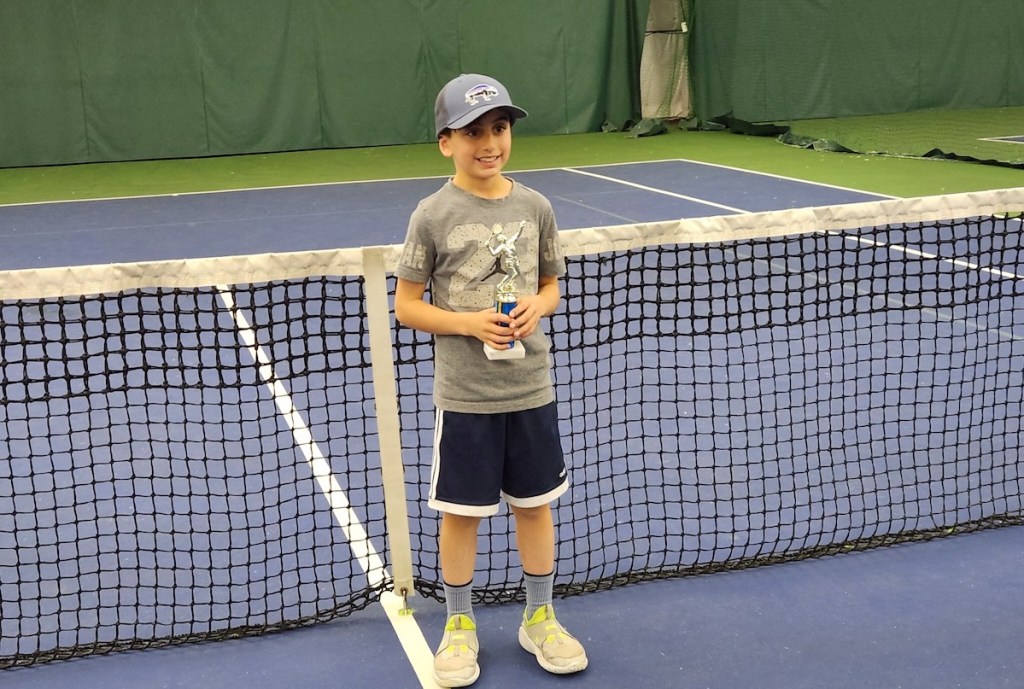 boy holding trophy on tennis court