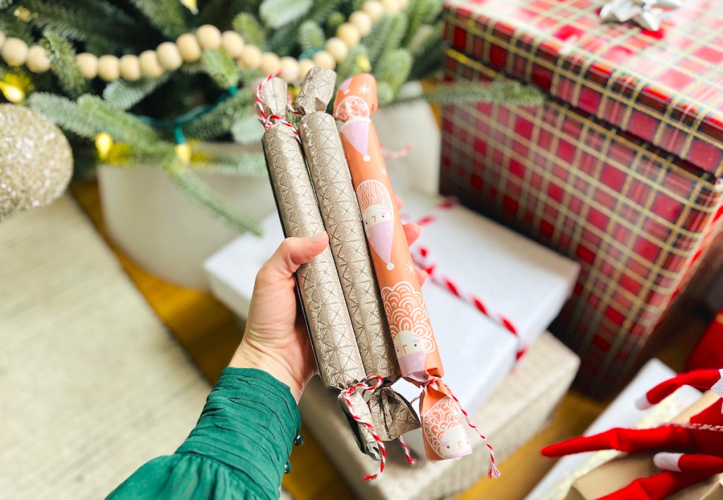 hand holding three rolled gifts in front of tree with gifts
