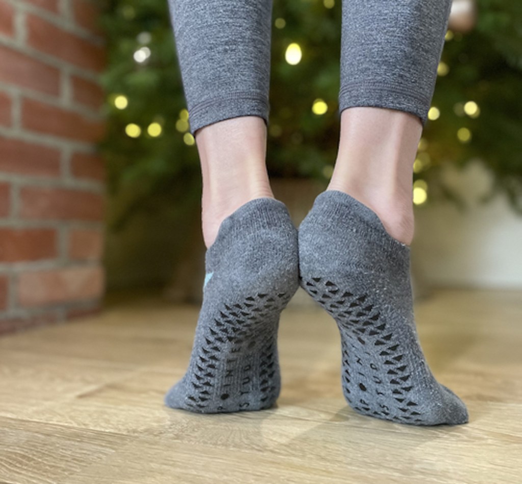 close up of feet wearing socks in front of lit christmas tree